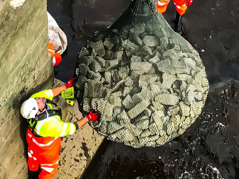 removing huge net bag of rocks from river by crane with man guiding
